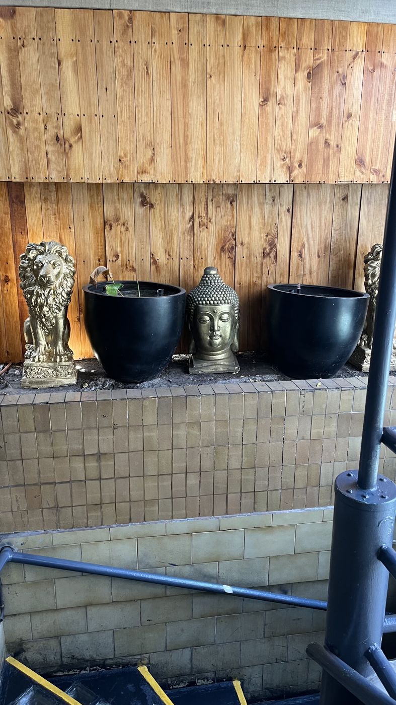Macetas negras vacías junto a estatuas de un buda y leones, en diciembre de 2024